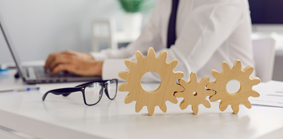 Three cogwheels joined together placed on desk against blurred background of busy office room