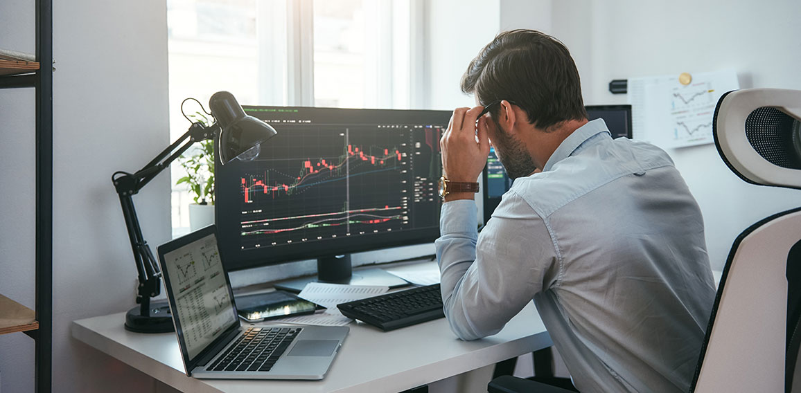 Working process. Smart male trader looking at charts on multiple computer screens and analyzing data while sitting in his modern office