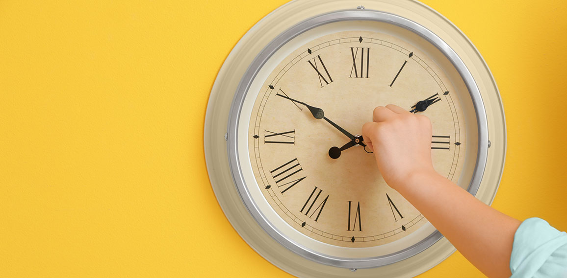 Little boy touching arrows of clock on color wall