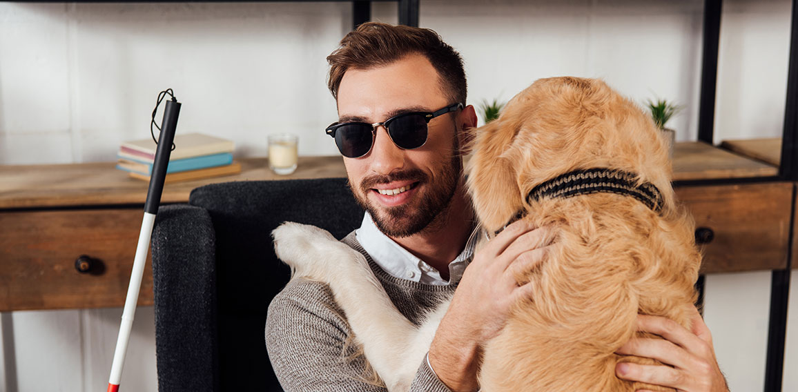 Smiling blind man sitting in armchair and hugging golden retriev