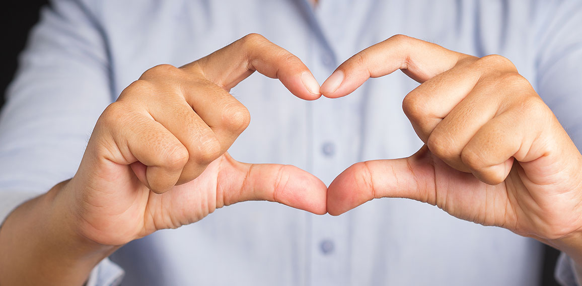 Man making heart figure love sign with fingers while standing in