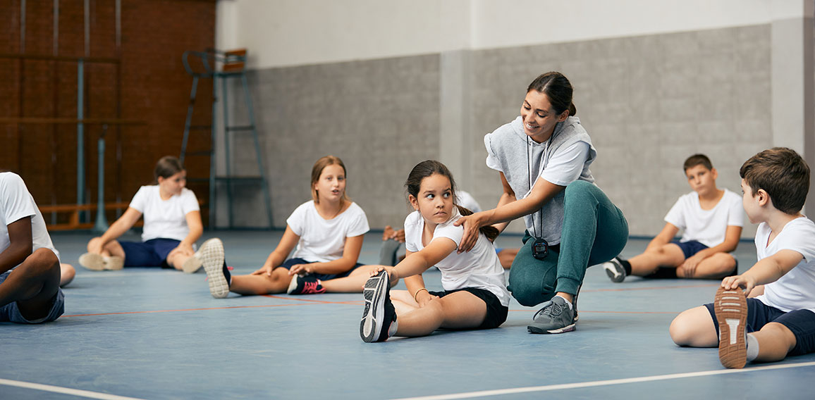 Happy female PE teacher having class with group of elementary students at school gym.