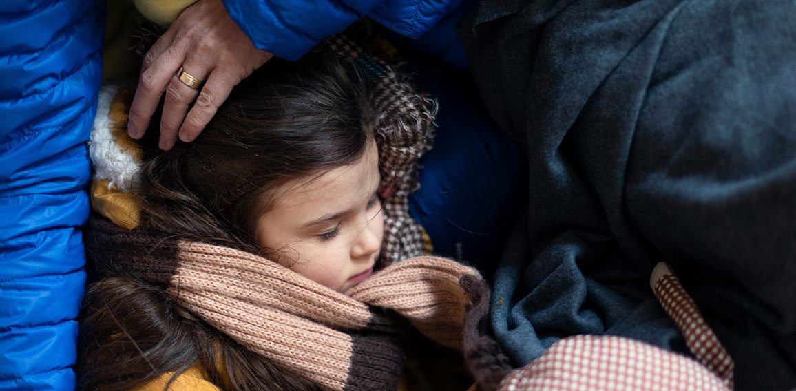 Ukrainian war refugees in temporary shelter and help center, little girl sleeping on her mother's lap.