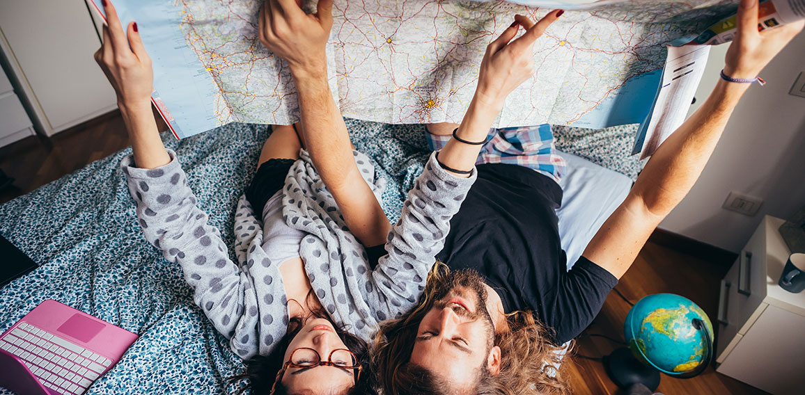 Young couple lying on bed planning travel reading map