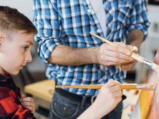 Little boy painting with father on canvas at home
