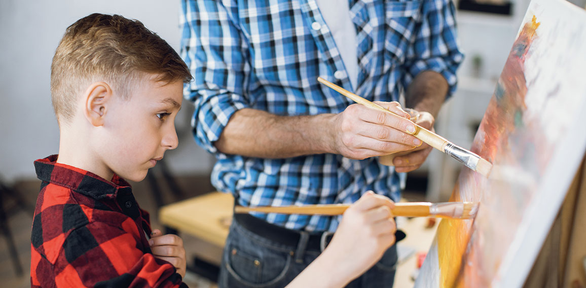 Little boy painting with father on canvas at home