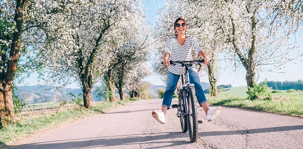 Happy smiling woman rides a bicycle on the country road under th