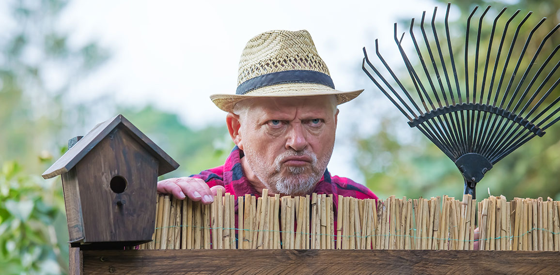 An elderly man with hat looks angry and watching over a garden f