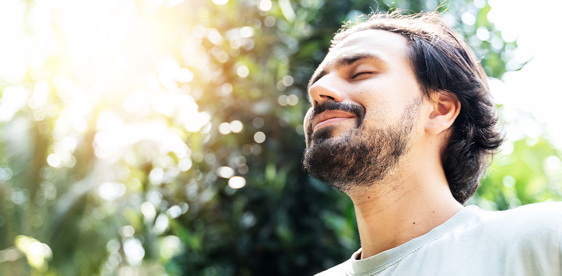 A bearded man is meditating outdoor in the park with face raised