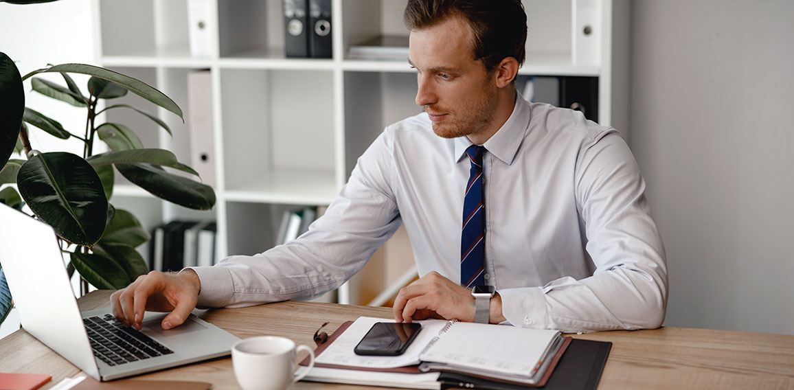 Man in shirt and tie using laptop while working