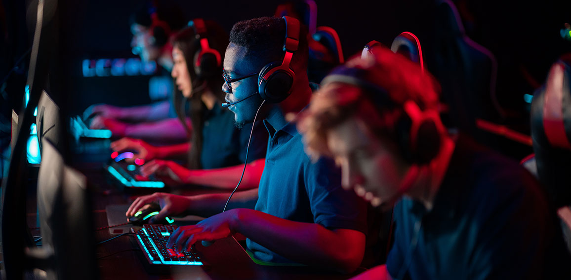 A multi-racial team of esports athletes conducts a training session before an online shooter tournament. Neon light.