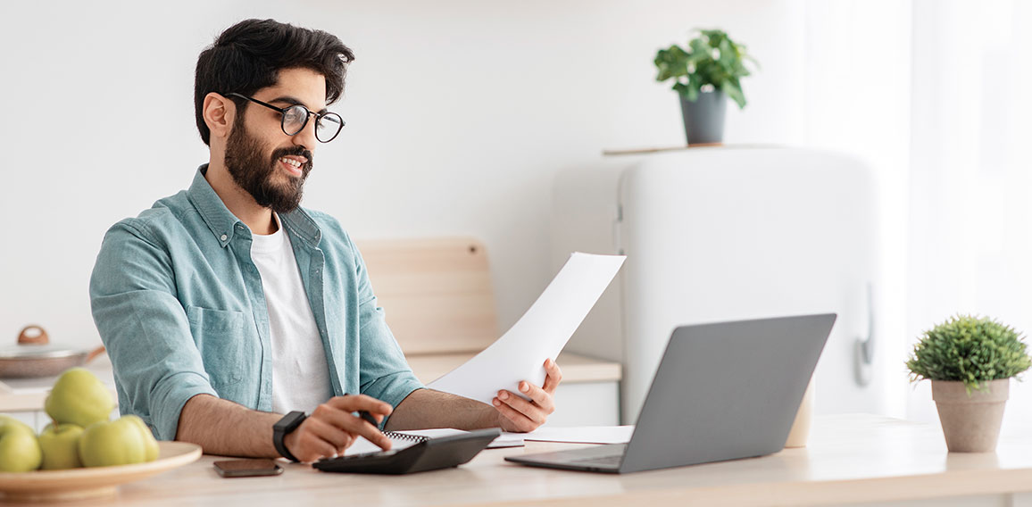 Savings and finances concept. Young arab guy using calculator and laptop computer, calculating taxes