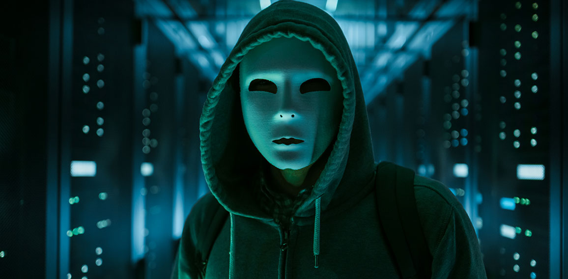 Masked Hacker in a Hoodie Standing in Corporate Data Center with