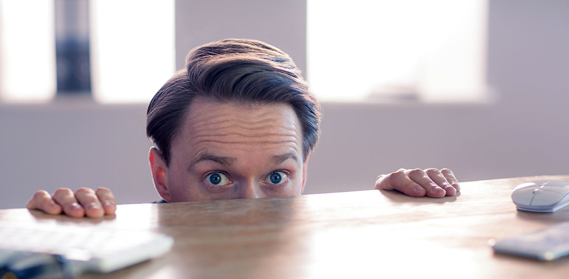 Nervous businessman peeking over desk