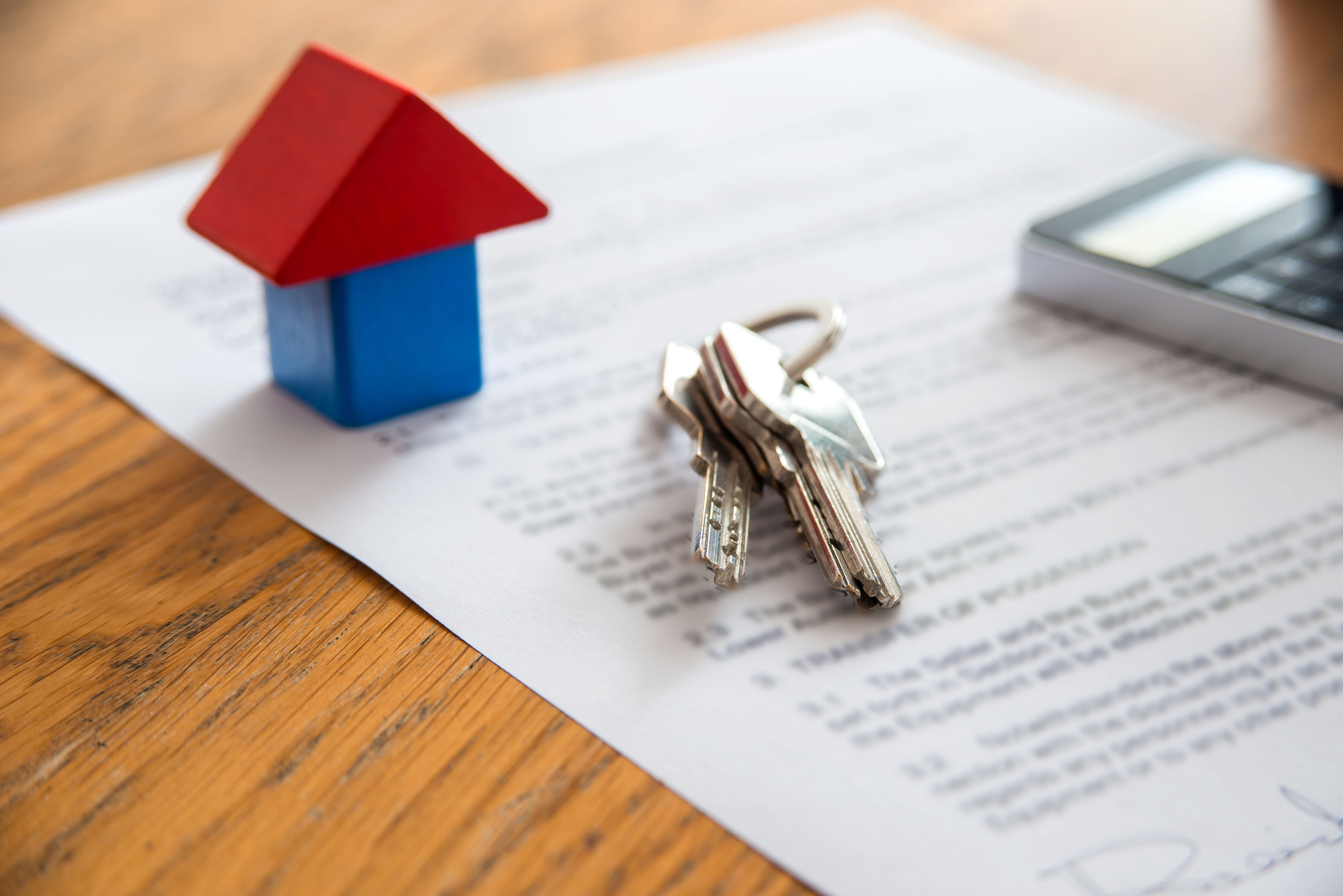 Wooden house miniature and house key lying on contract