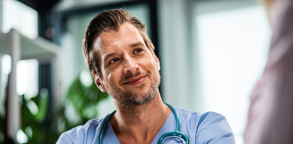 Smiling male doctor talking to his patient while going through medical reports at his office.