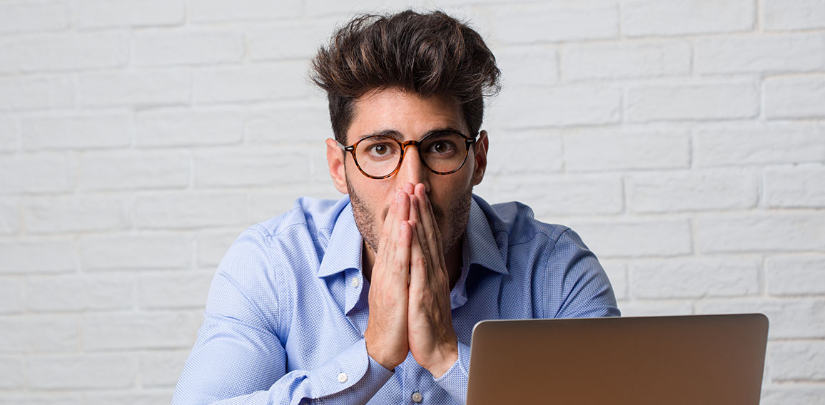 Young business man sitting and working on a laptop very scared and afraid, desperate for something, cries of suffering and open eyes, concept of madness