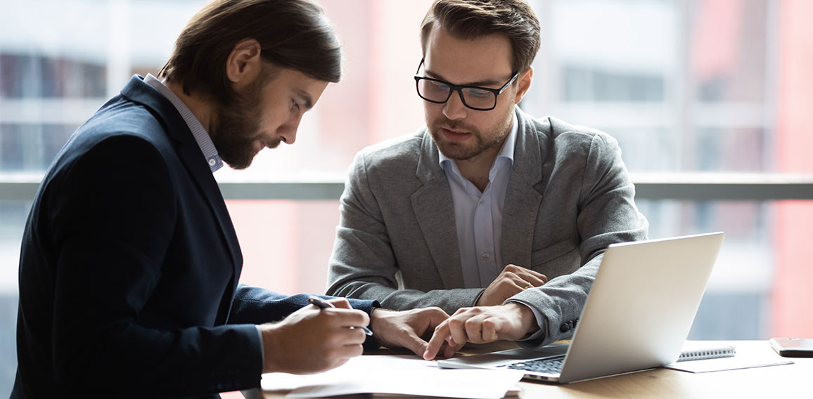 Focused young businessman signing agreement with skilled lawyer.