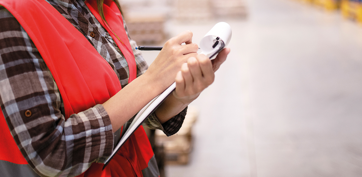 Woman warehouse worker leaning on cardboard boxes and taking not