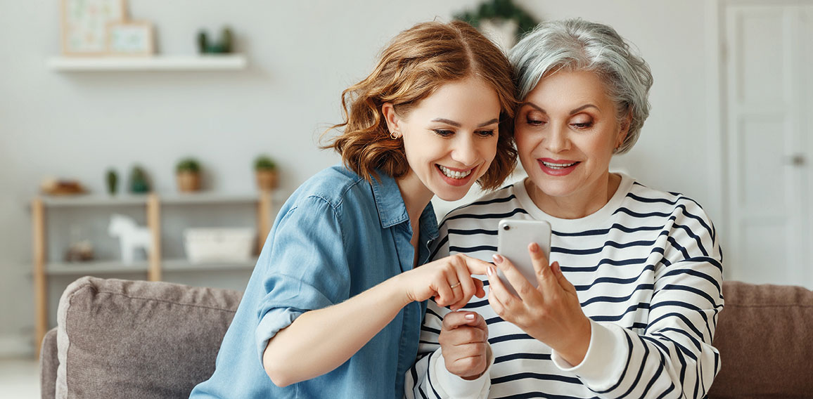 Cheerful mother and daughter using smartphone on sofa