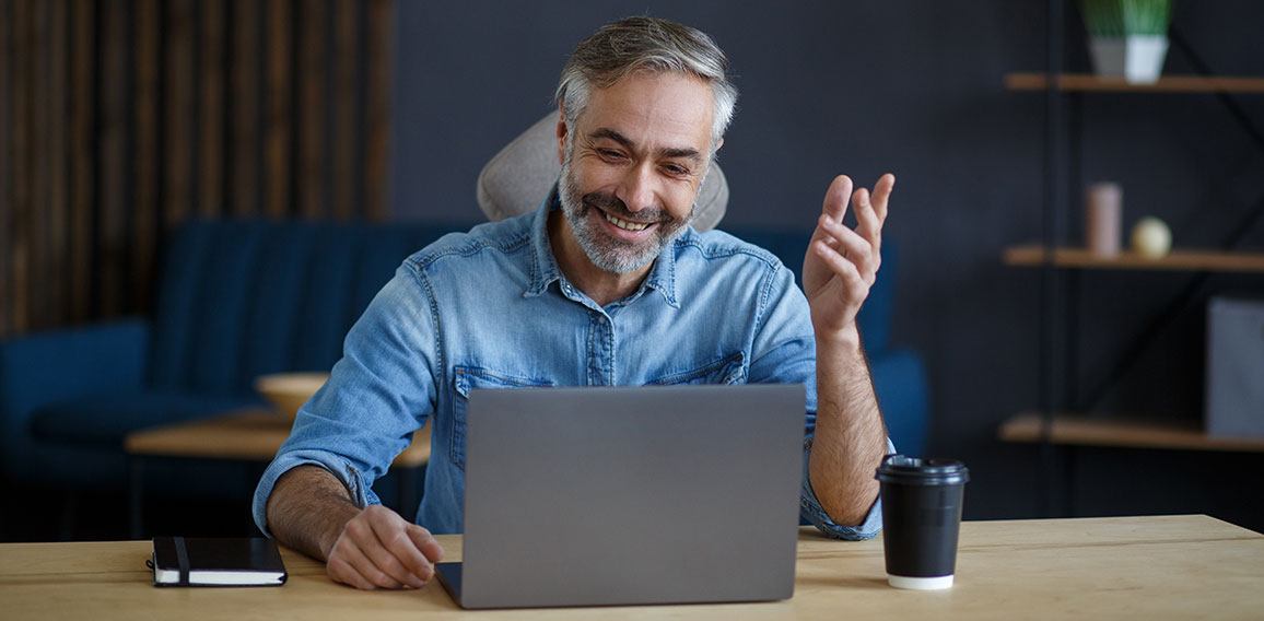 Portrait of grey-haired senior handsome smiling man working from home. Communication online with colleagues and video conference. Online meeting, video call, remote working