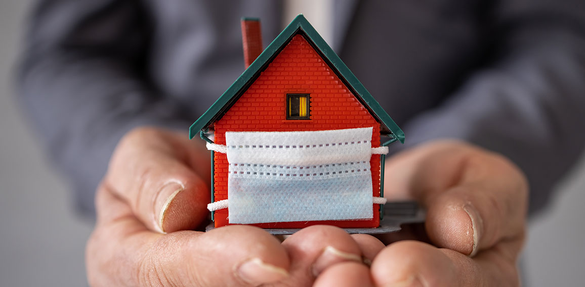 Senior businessman holding model house wearing protective medica