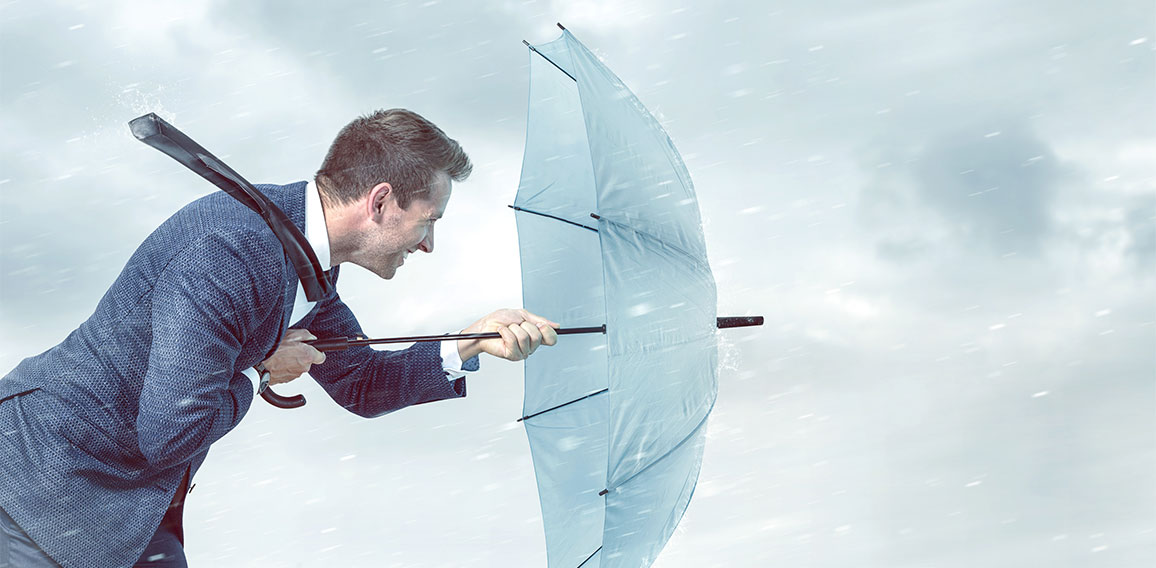 Businessman with an umbrella is facing strong headwind