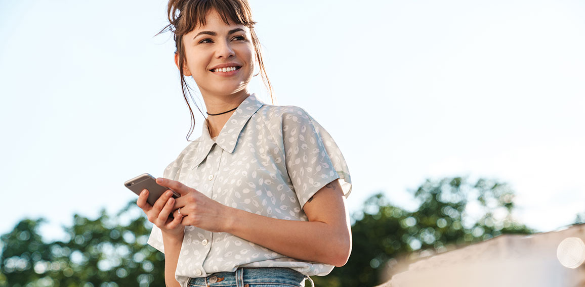 Positive cheery happy young beautiful woman on a balcony using mobile phone chatting.