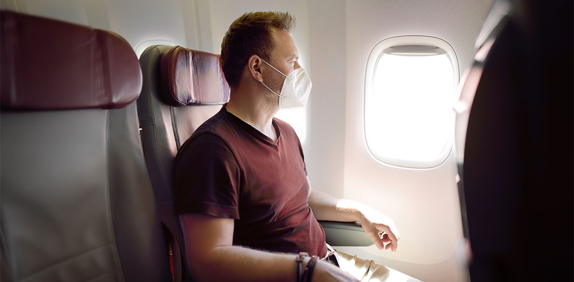 Middle age man in face mask traveling by an airplane. Passenger sitting in aircraft and looking on plane window during flight. Safety and protection of fly transportation while coronavirus