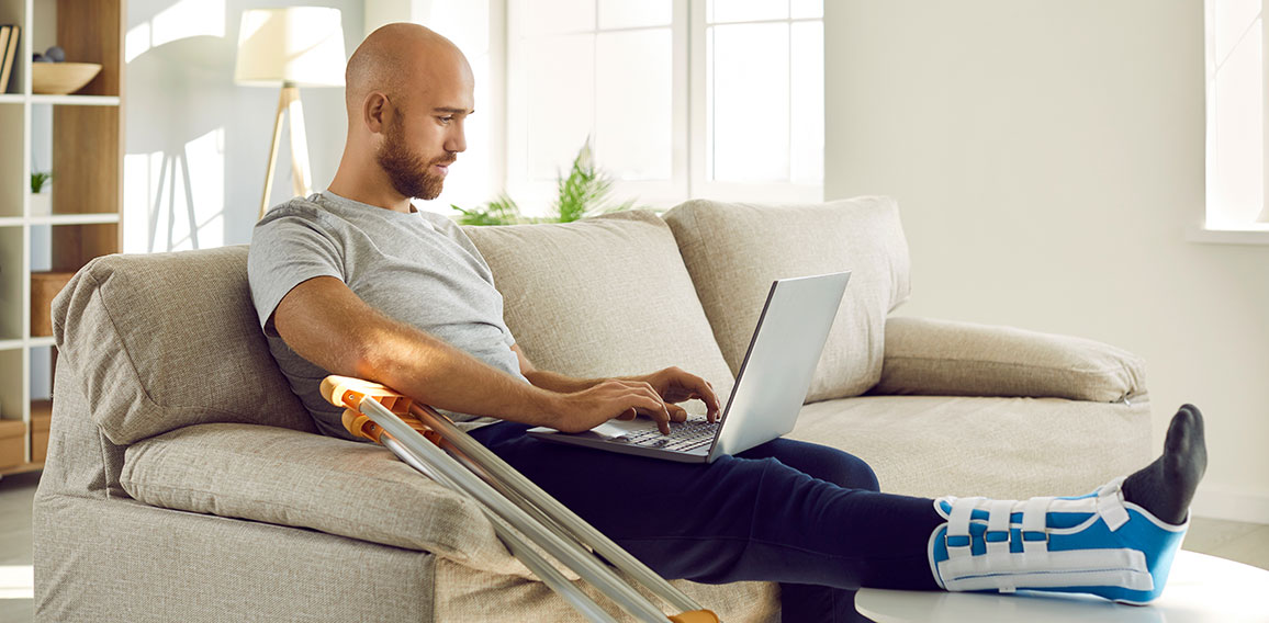 Unwell man with broken leg work on computer