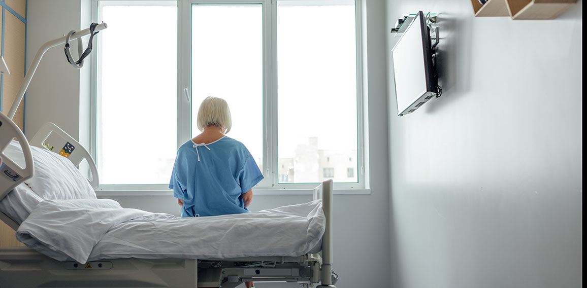 back view of lonely senior woman sitting on bed in hospital ward