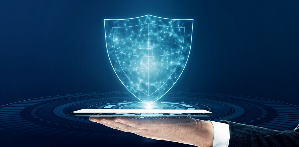 Close up of businessman hand holding tablet with glowing polygonal shield on blue background. Secure and safety concept.