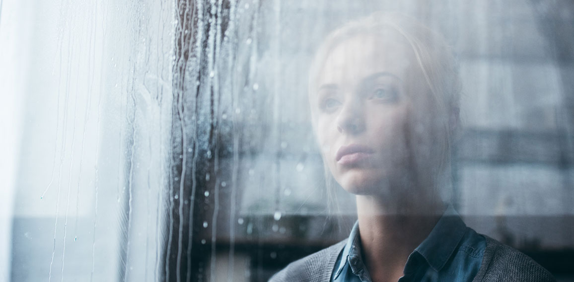 selective focus of sad adult woman at home looking through windo