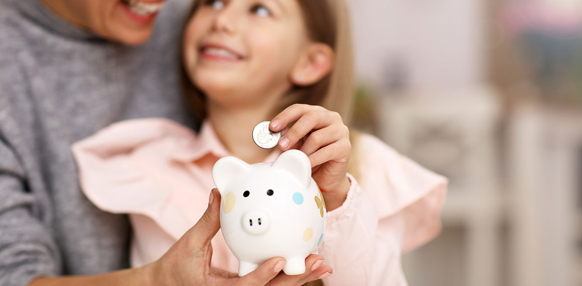 Young girl and her mother with piggybank sitting at table