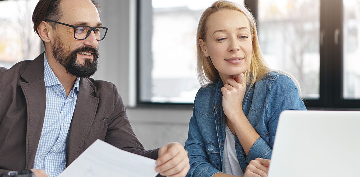 Successful mature bearded businessman and his colleague work together in office, discuss statistics. Young female shows presentation on laptop computer to her boss, going show it on business meeting