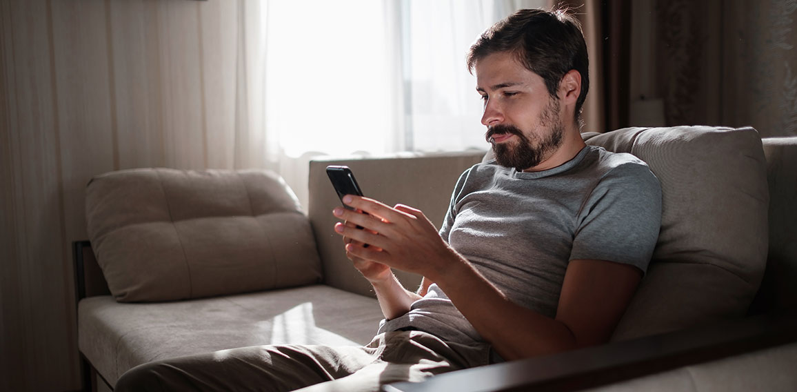 Portrait of an attractive smiling young bearded man wearing casual clothes sitting on a couch