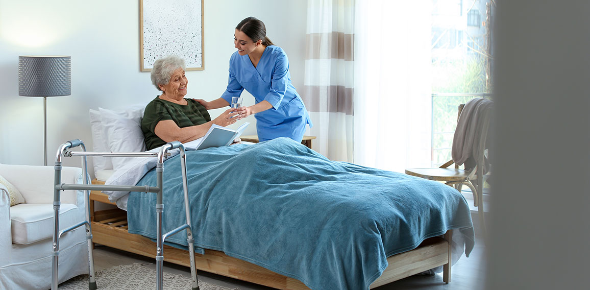 Care worker giving water to elderly woman in geriatric hospice