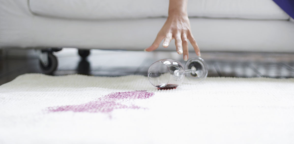 Midsection of woman reaching toward spilled wine glass on rug