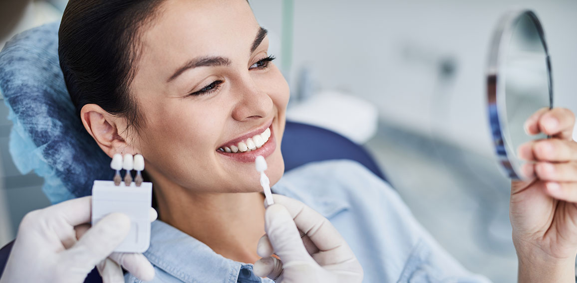 Male dentist comparing color of lady teeth with sample