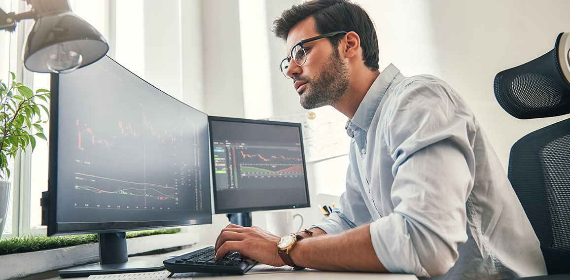 Confident businessman. Young bearded trader in formal wear is analyzing trading charts on computer screens while sitting in his modern office