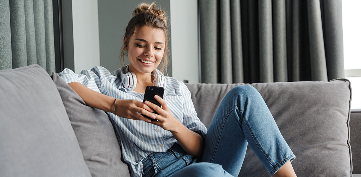 Image of smiling nice woman using cellphone while sitting on sof