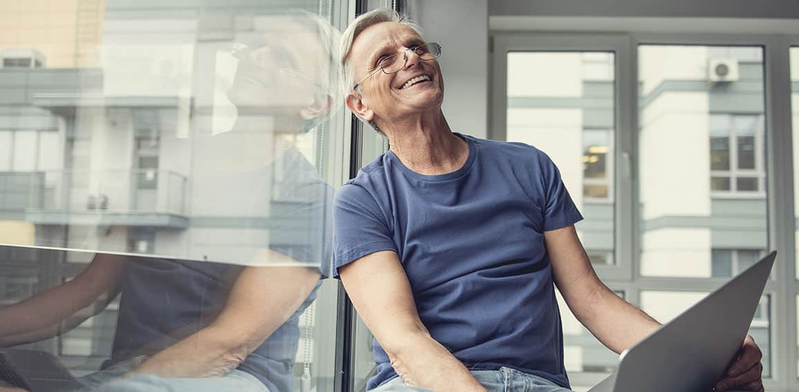 Happy elderly man sitting with gadget on knees