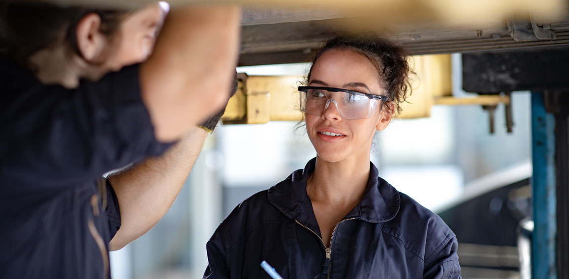 Hispanic Female trainee Mechanics Working Underneath Car Togethe