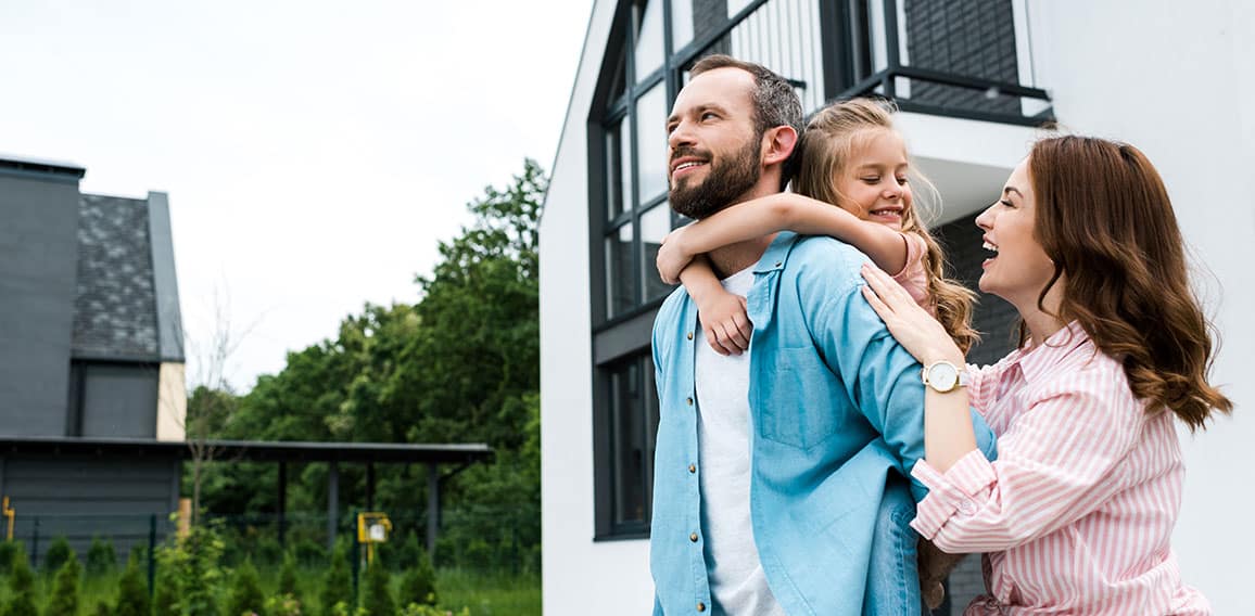 happy man piggybacking daughter near cheerful wife and house