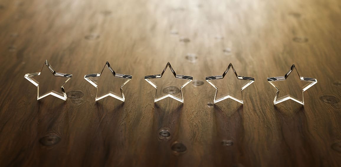 3D render: Five star rating - five transparent acrylic glas stars standing on a wooden table. Selective focus and copy space.