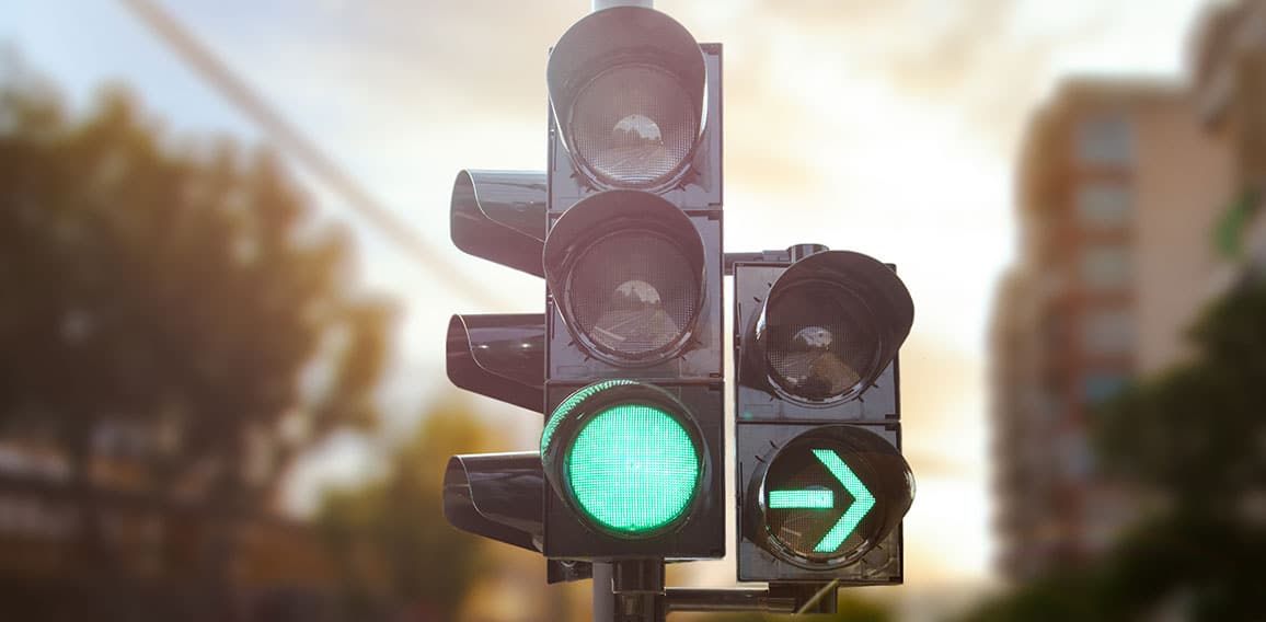 Green traffic light with green arrow light up in city while suns