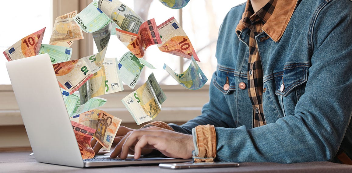 Man with modern laptop and flying euro banknotes at table indoor