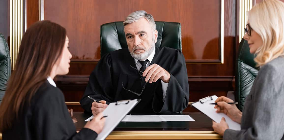 senior judge holding eyeglasses near attorney and prosecutor writing on clipboards