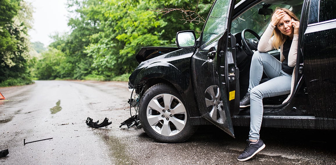 Young woman in the damaged car after a car accident, making a phone call.