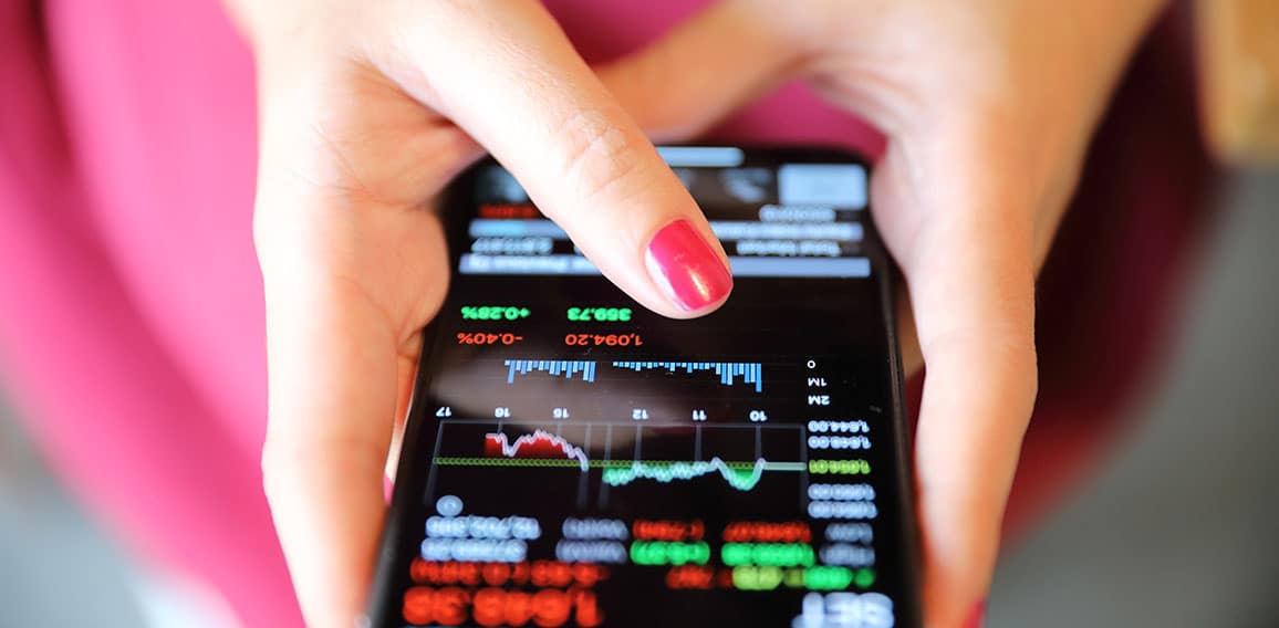 Female hand with smartphone trading stock online in coffee shop